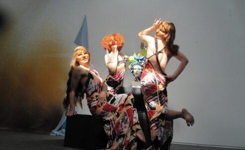 Three people in wildly printed dresses pose before a white backdrop