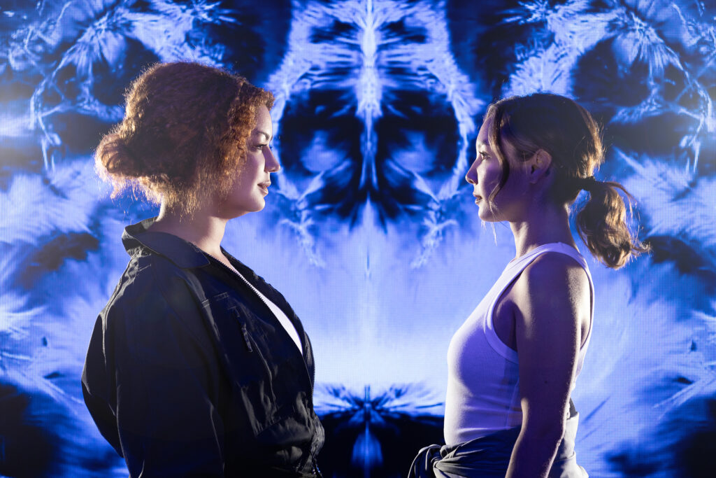 Two people standing face to face with one another front of a blown up xray style image of a human brain