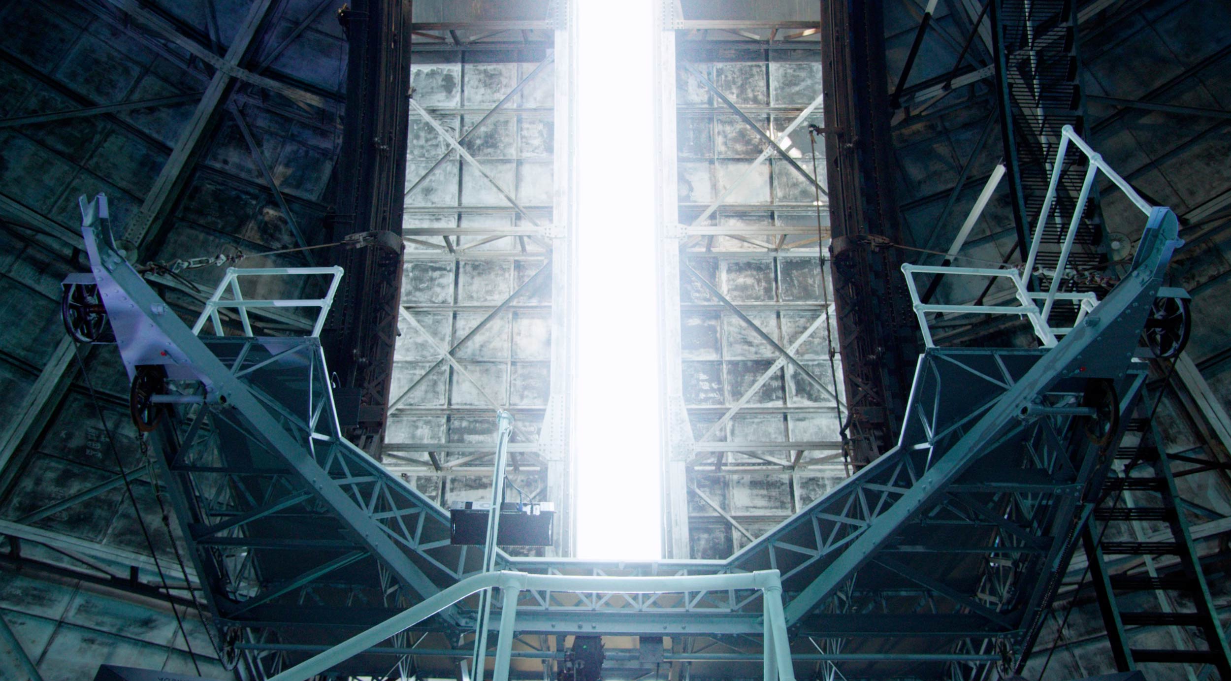 symmetrical image with a vertical beam of light at the center behind a scaffolding