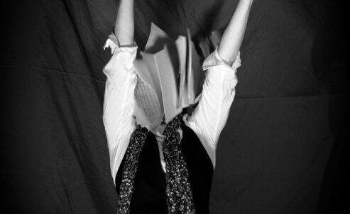 thin person wearing a vest with their arms thrown into the air and pages of a book where their head would be